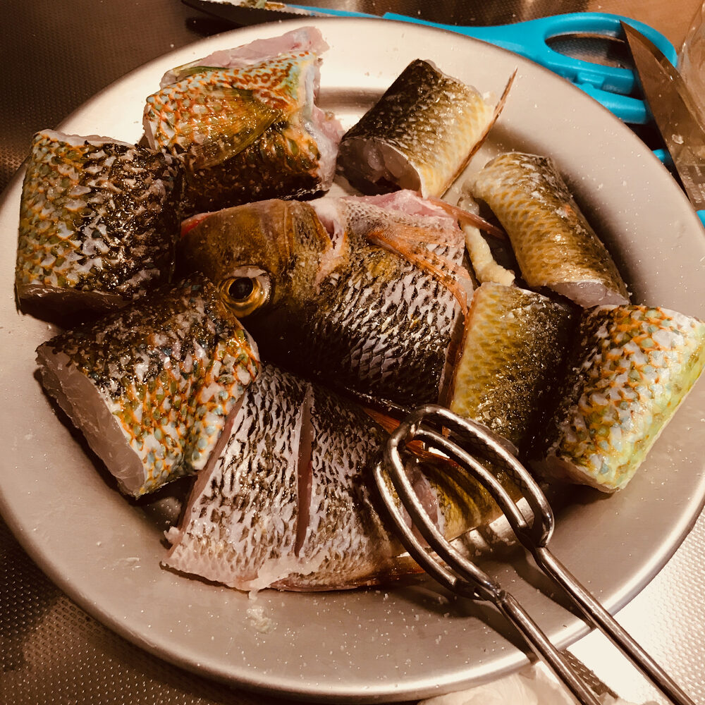 丸い金属の皿に積んだ、皮つきの魚の切り身とトング