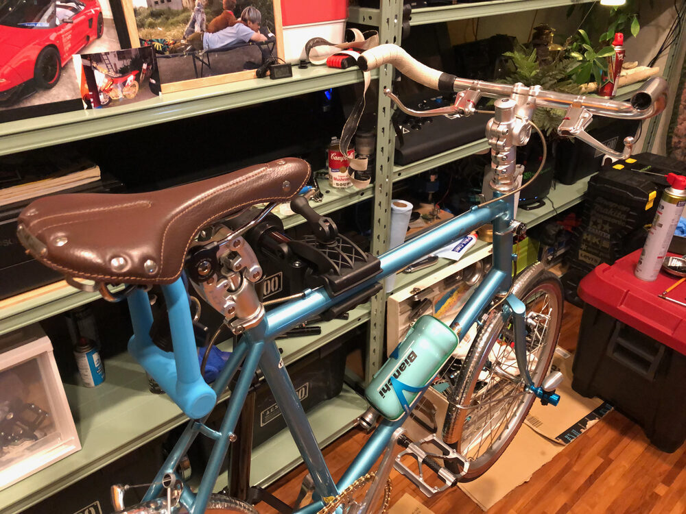 夜に撮った、茶色い革のサドルと水色のフレーム、奥の工具棚