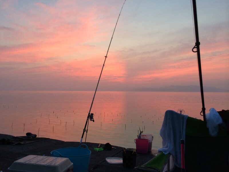 夕焼けの海に釣り竿が並ぶ堤防