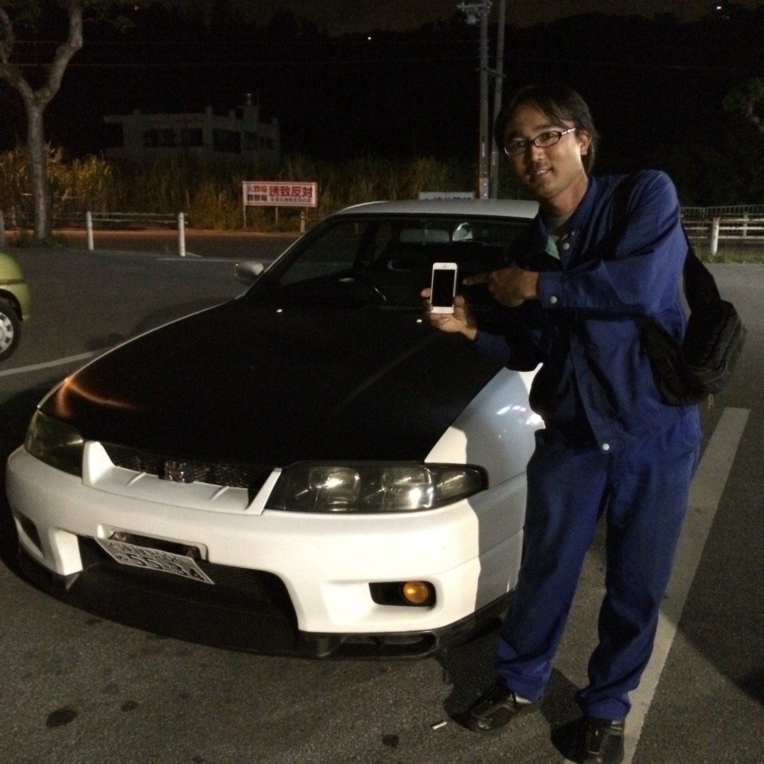 直ったiPhoneを指さす宮平さんと愛車のスカイライン